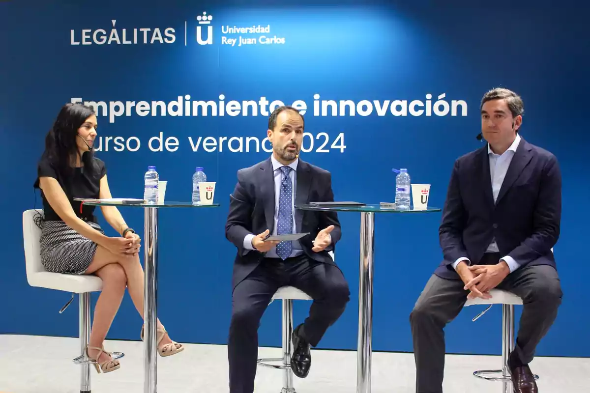 Tres personas sentadas en taburetes altos participando en un evento sobre emprendimiento e innovación organizado por la Universidad Rey Juan Carlos y Legálitas.