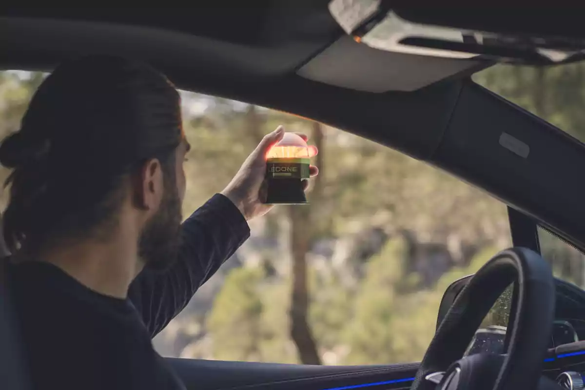 Un hombre dentro de un coche sostiene un dispositivo luminoso cerca de la ventana.