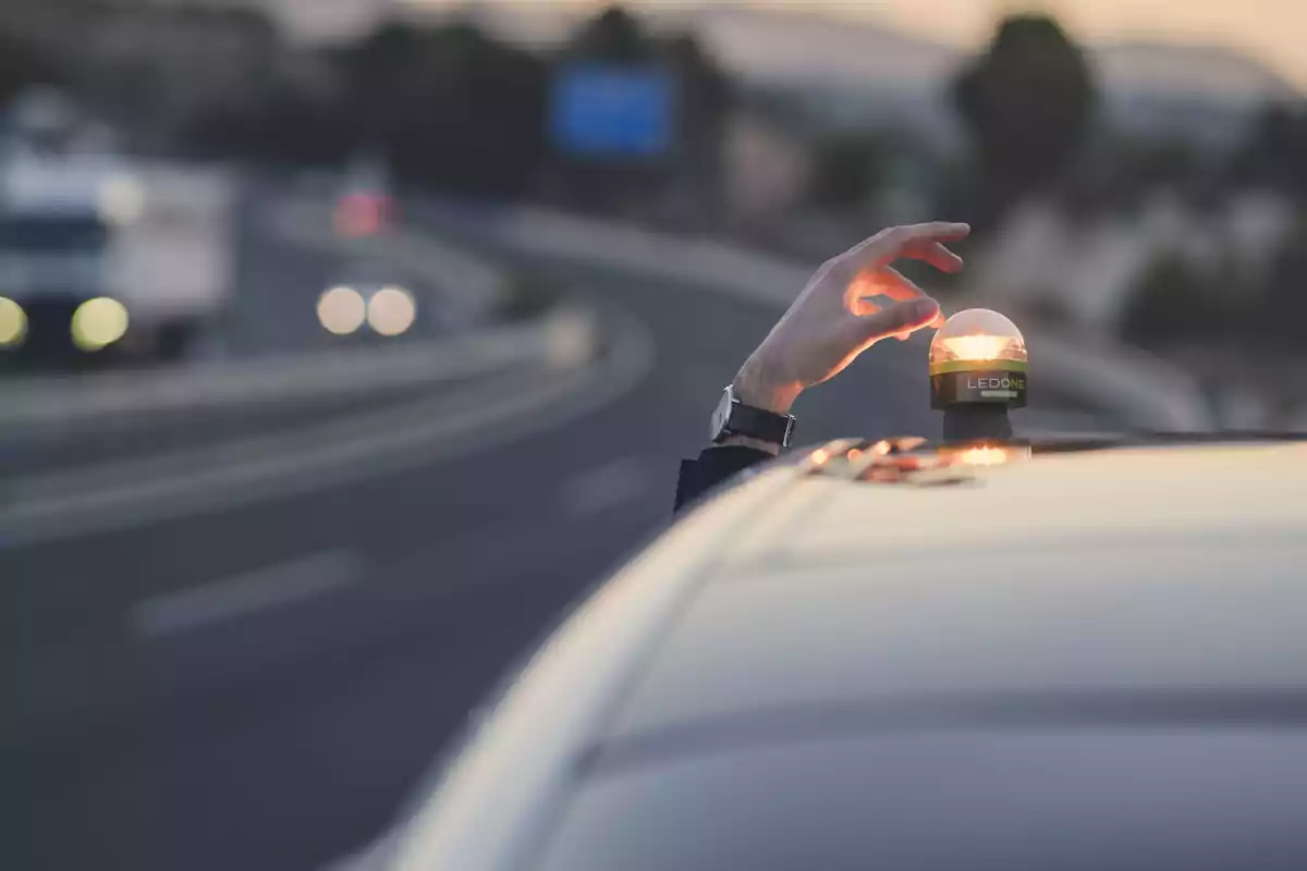 Una mano colocando una luz de emergencia LED sobre el techo de un automóvil en una carretera.