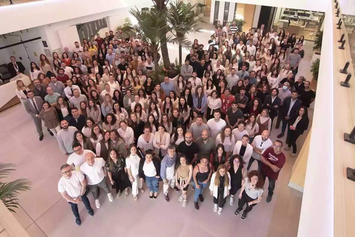 Un gran grupo de personas posando juntas en el interior de un edificio moderno con una planta en el centro.