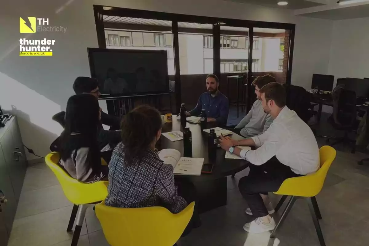 Un grupo de personas en una reunión de trabajo en una sala de conferencias con sillas amarillas y una pantalla grande.