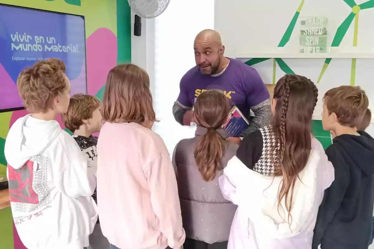 Un hombre hablando con un grupo de niños en un entorno educativo colorido.