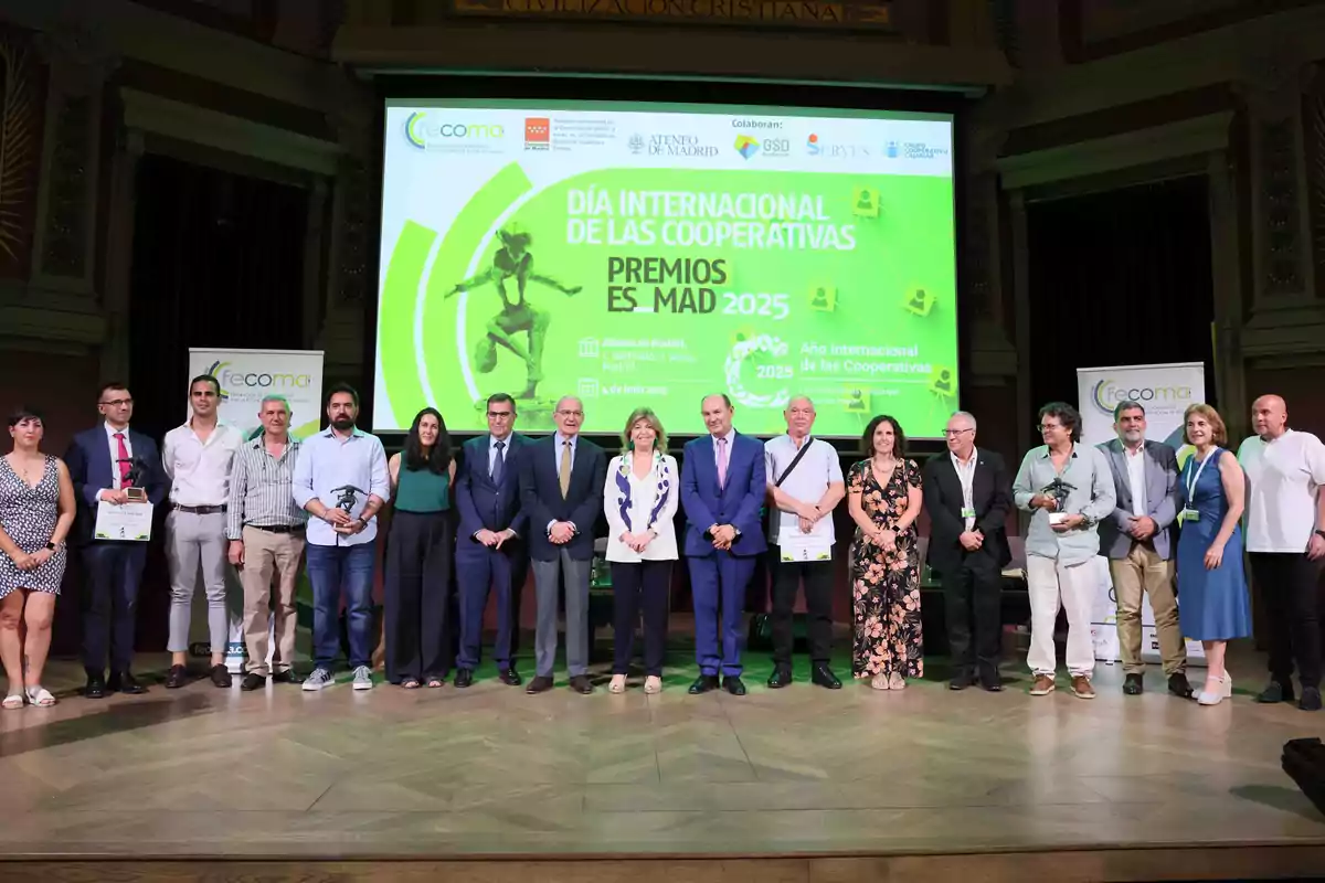 Grupo de personas posando en un escenario durante la celebración del Día Internacional de las Cooperativas con un cartel verde de fondo que anuncia los premios ES MAD 2025