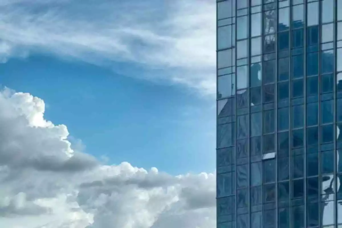 Edificio de cristal reflejando el cielo azul con nubes blancas