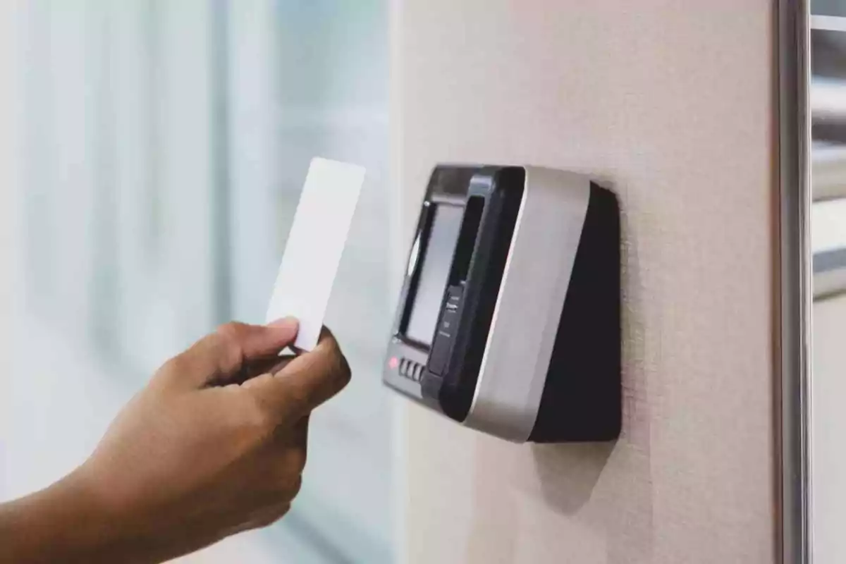 Persona acercando una tarjeta a un lector de control de acceso en la pared