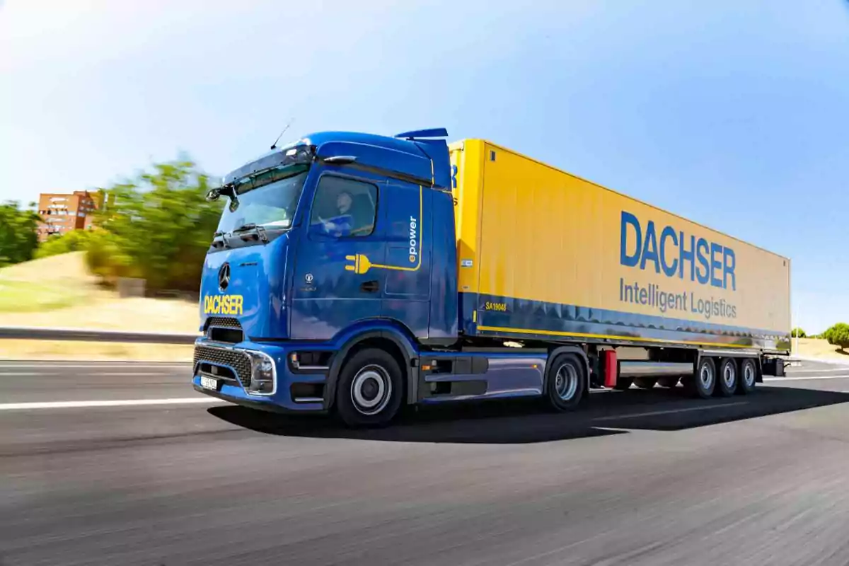 Camión de carga azul y amarillo de la empresa Dachser circulando por una carretera en un día soleado
