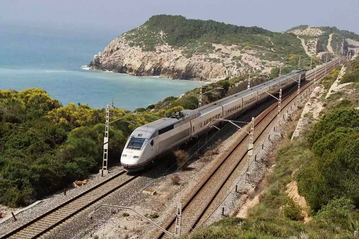 Tren de alta velocidad circulando junto a la costa con el mar y montañas al fondo