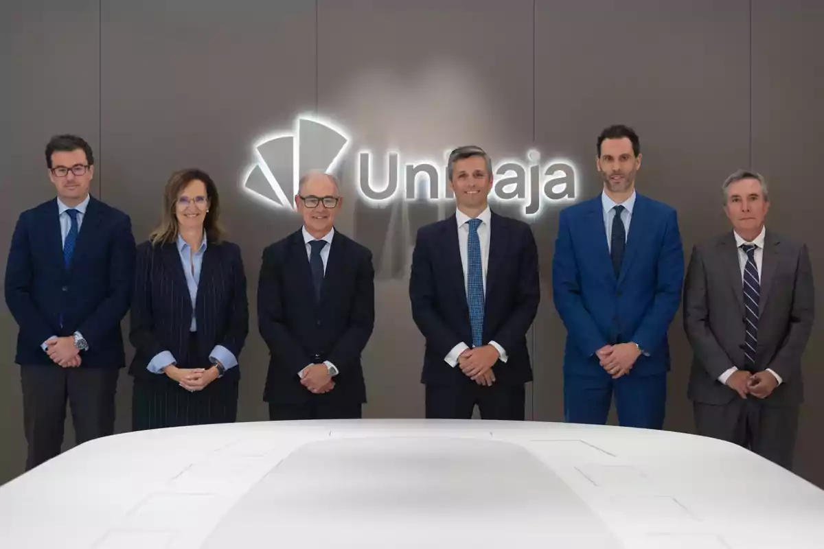 Seis personas vestidas de traje posan frente a una pared con el logotipo de Unicaja