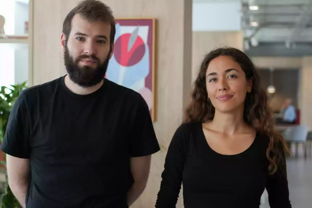 Dos personas jóvenes con ropa negra posan en un entorno de oficina moderno