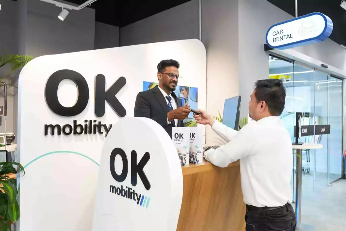 Un hombre entrega las llaves de un coche a un cliente en el mostrador de una oficina de alquiler de autos de OK Mobility