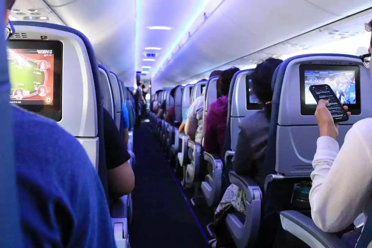 Pasajeros sentados en la cabina de un avión, algunos usando pantallas y dispositivos móviles durante el vuelo