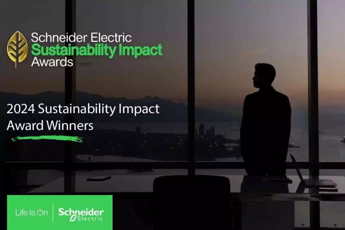 Persona de pie junto a una ventana grande con vista a la ciudad al atardecer y texto sobre los ganadores de los premios de impacto en sostenibilidad 2024 de Schneider Electric