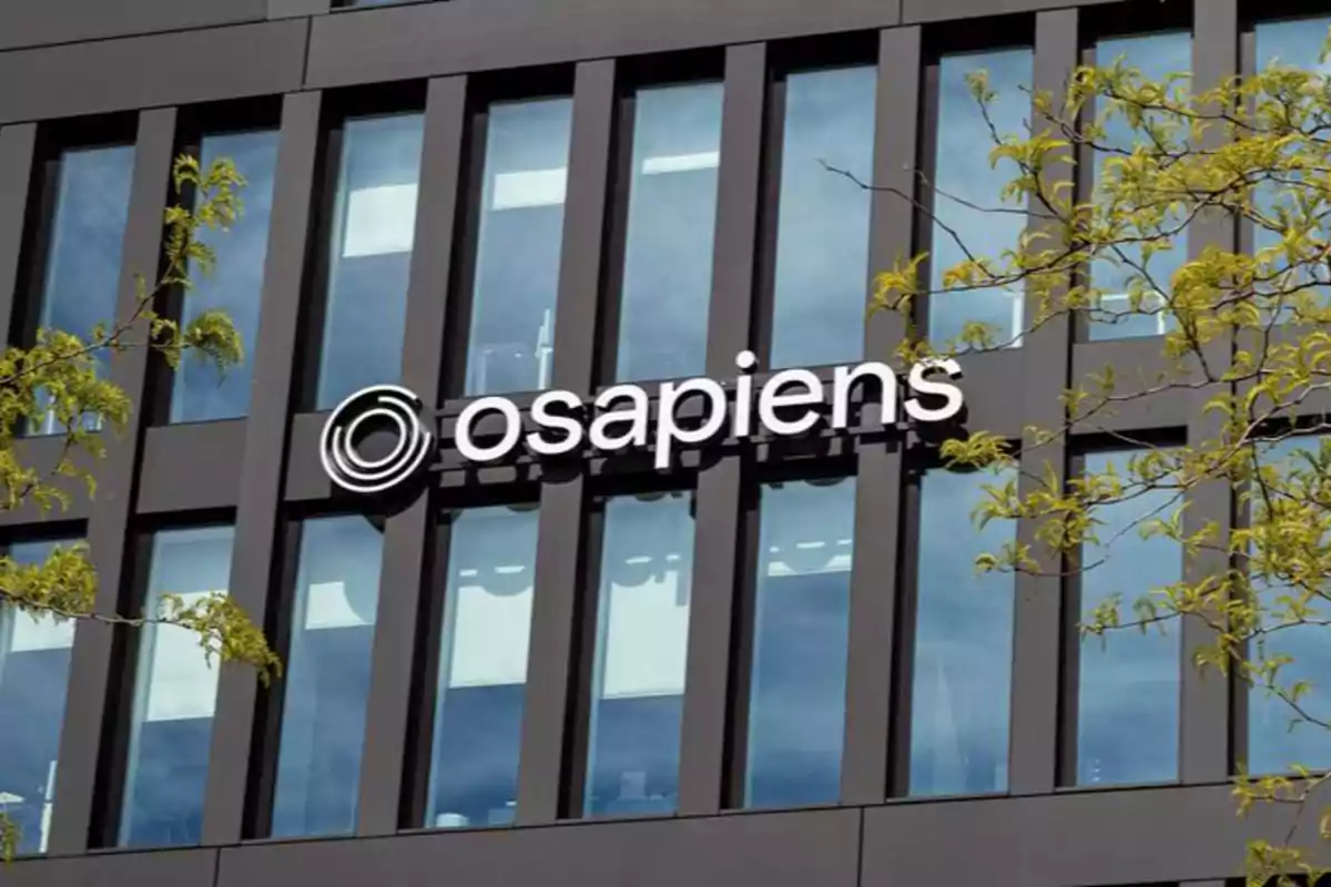 Fachada de edificio moderno con el logo de osapiens y ramas de árbol en primer plano