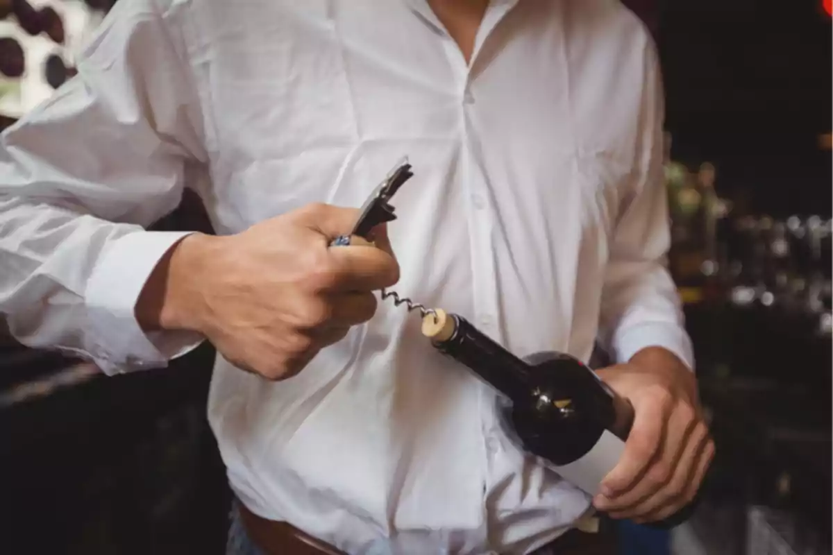 Persona con camisa blanca abriendo una botella de vino con un sacacorchos