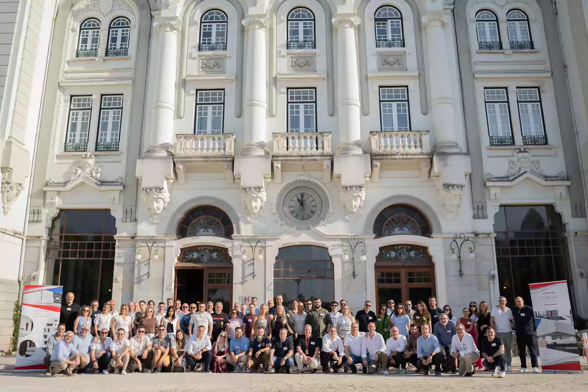 Grupo numeroso de personas posando frente a un edificio antiguo de fachada blanca con grandes ventanas y columnas