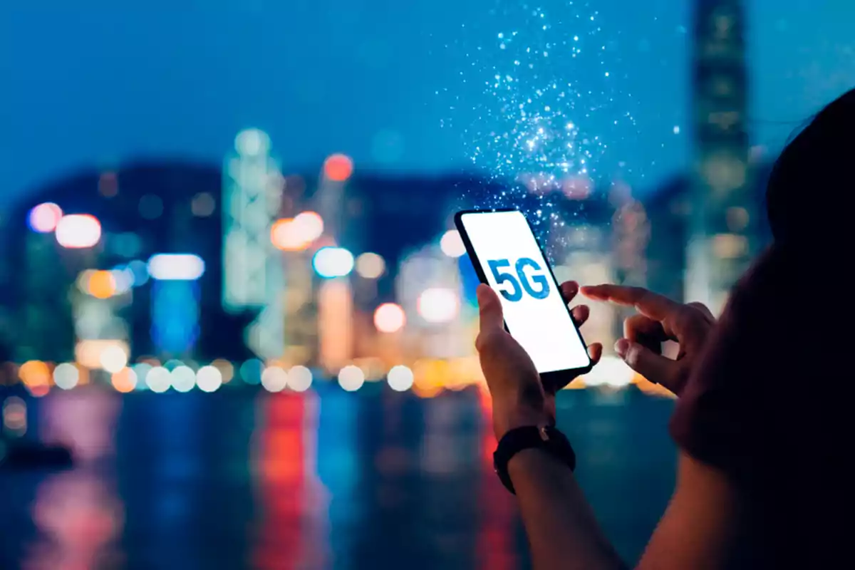 Persona usando un teléfono inteligente con la pantalla que muestra 5G y una ciudad iluminada de fondo