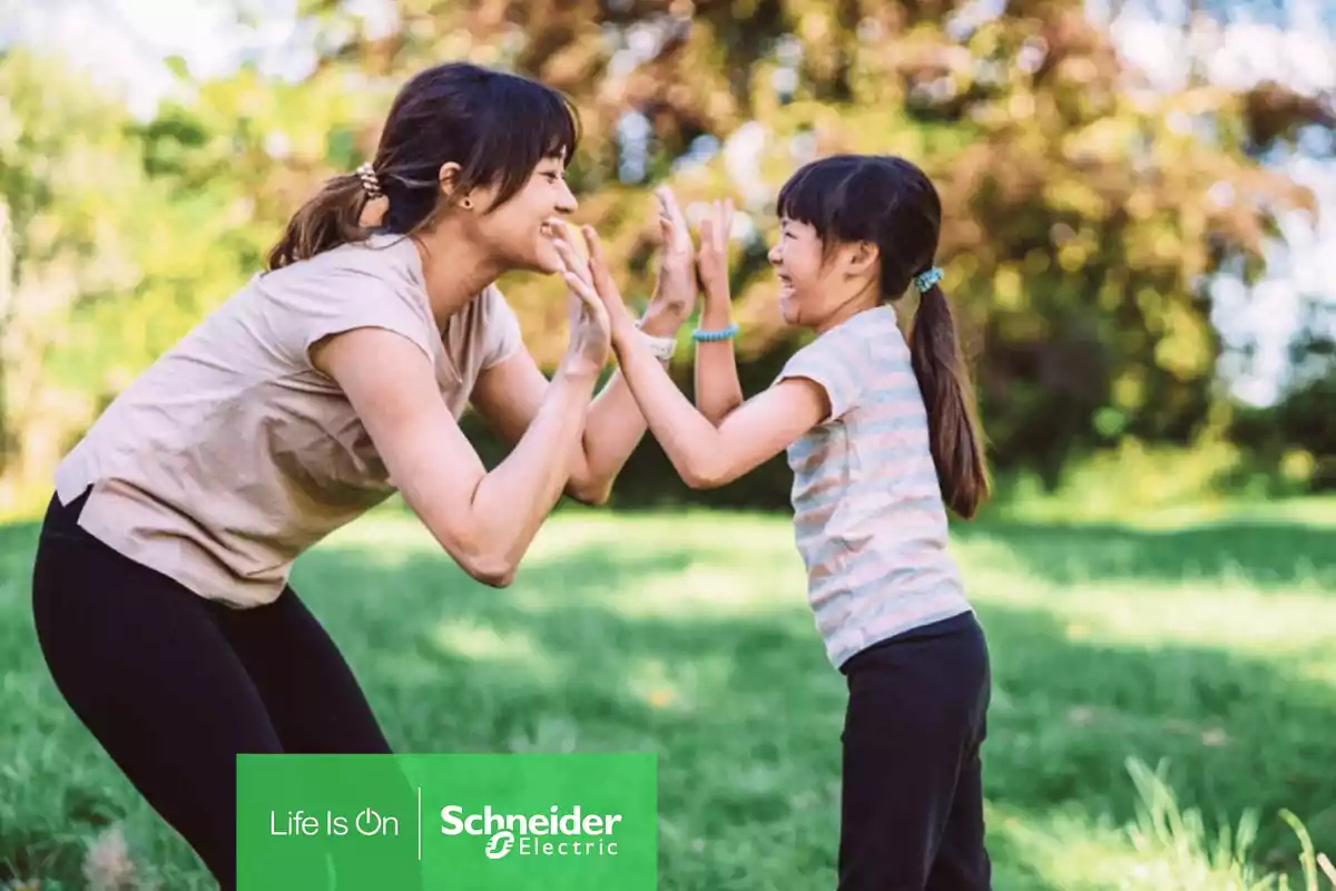Mujer y niña juegan y sonríen al aire libre en un parque con el logo de Schneider Electric en la esquina inferior izquierda