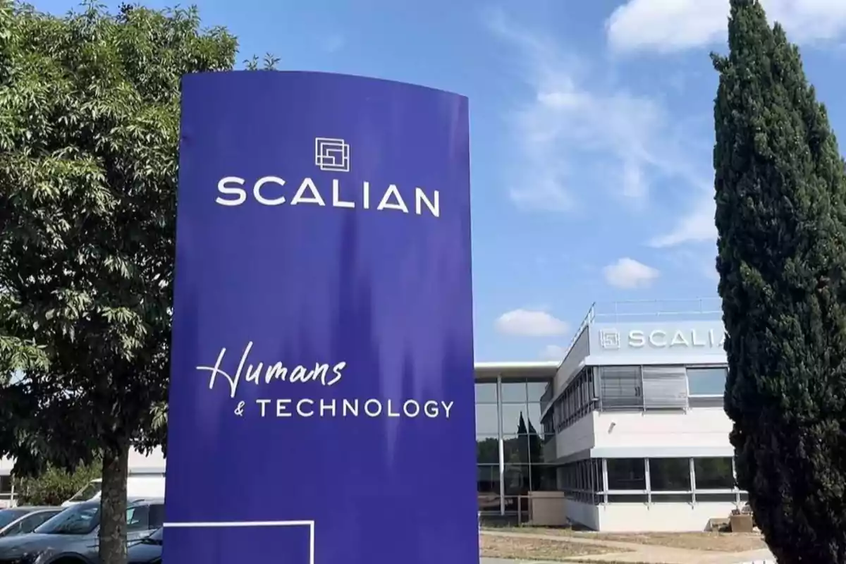 Edificio moderno de oficinas con un letrero grande de color azul que tiene el logo y nombre de Scalian junto al eslogan Humans & Technology rodeado de árboles y cielo despejado
