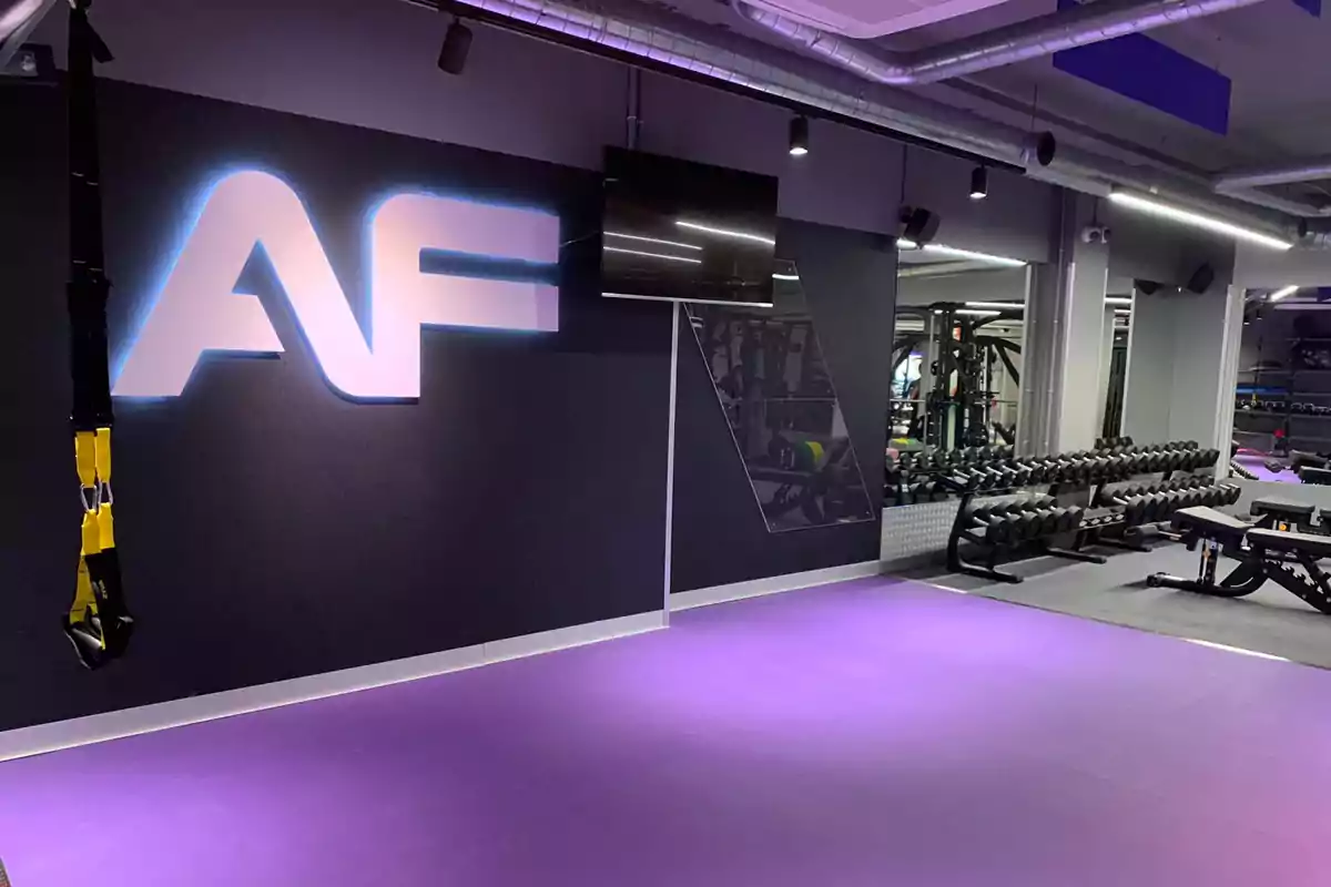 Gimnasio moderno con piso morado, logo AF en la pared, pesas alineadas y equipo de entrenamiento funcional