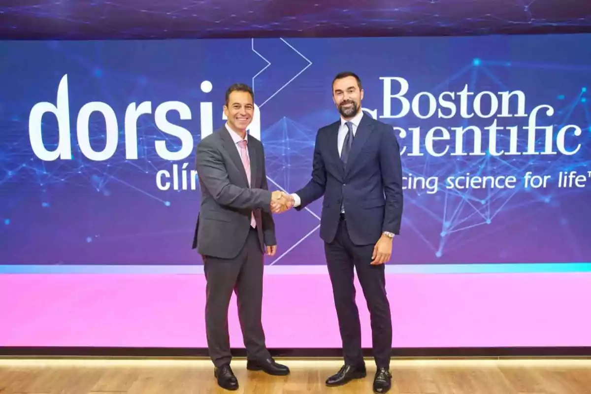 Dos hombres de negocios vestidos con traje se dan la mano frente a un fondo con los logotipos de Dorsia y Boston Scientific