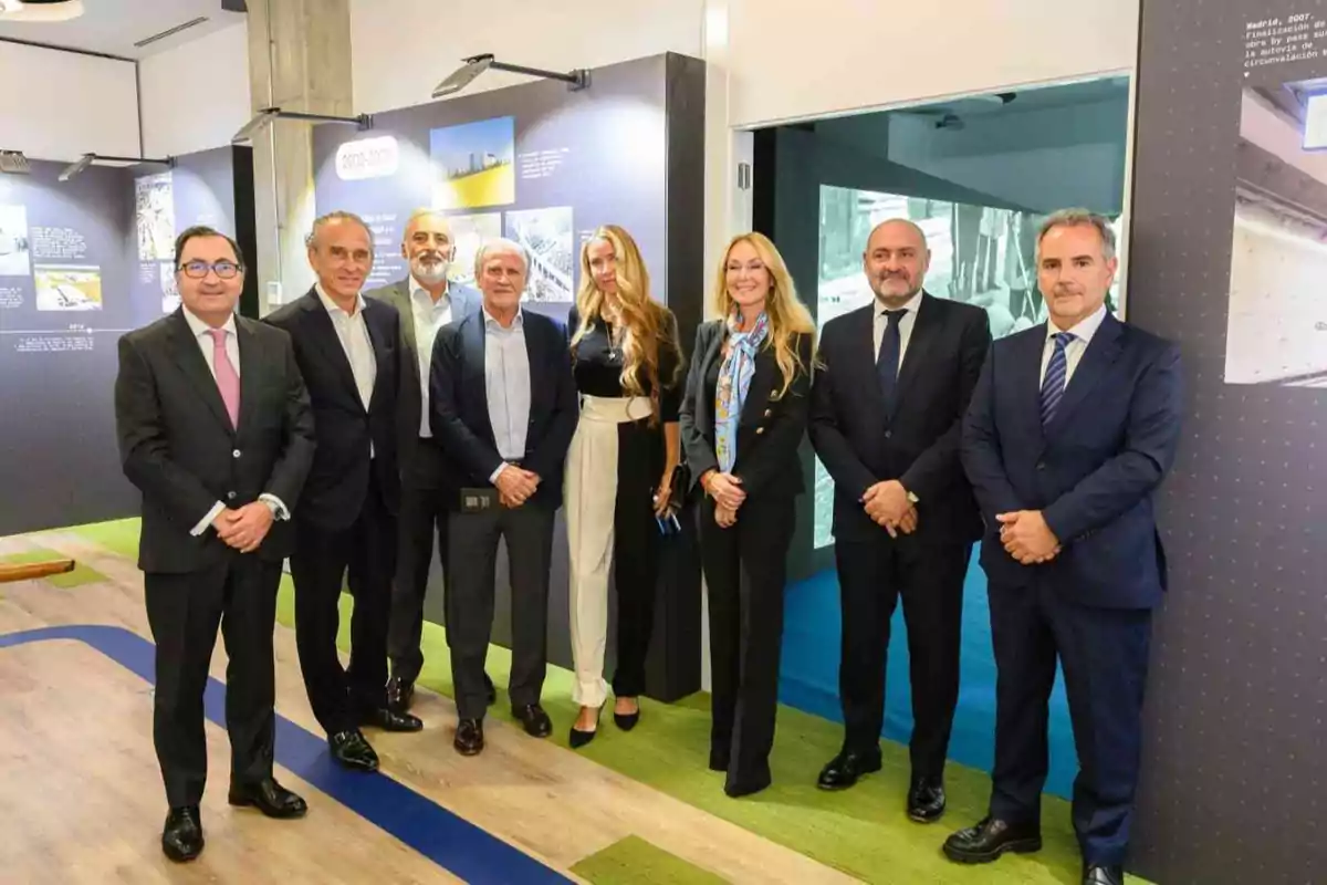 Ocho personas posan de pie en un entorno profesional con paneles informativos al fondo, todos vestidos con ropa formal y sonriendo a la cámara.