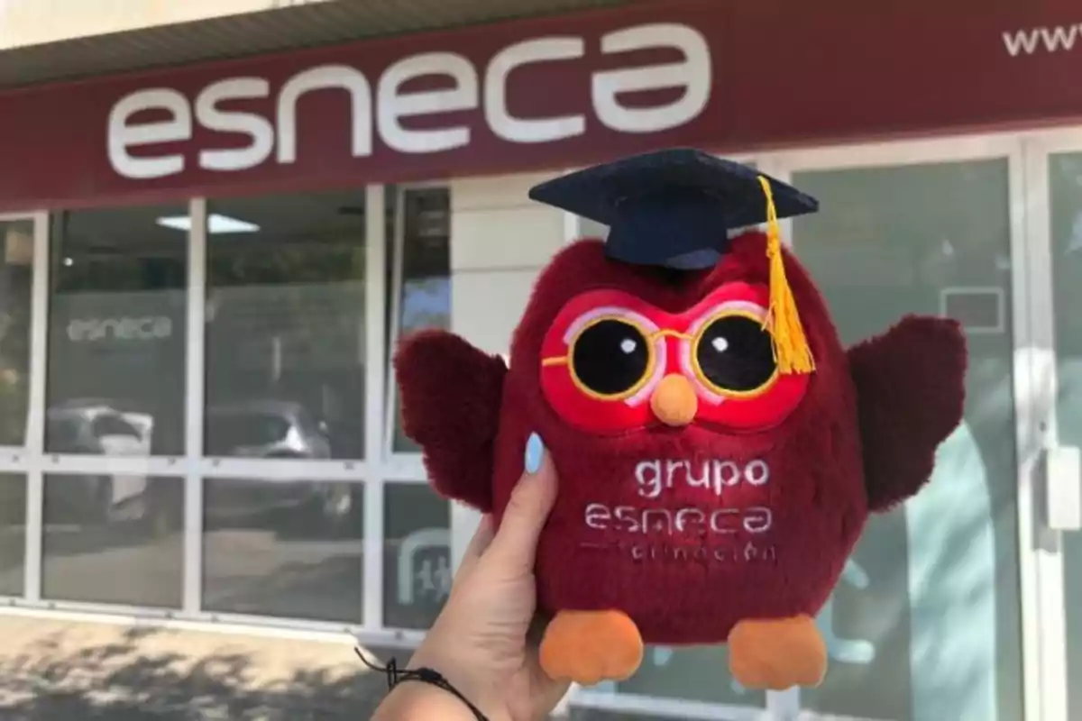 Persona sostiene un peluche de búho con birrete frente a un edificio con el letrero de esneca