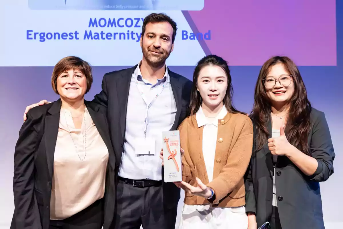 Cuatro personas sonríen en el escenario mientras una de ellas sostiene un trofeo de premio y otra muestra un pulgar arriba, con un fondo que muestra el nombre de un producto ganador.