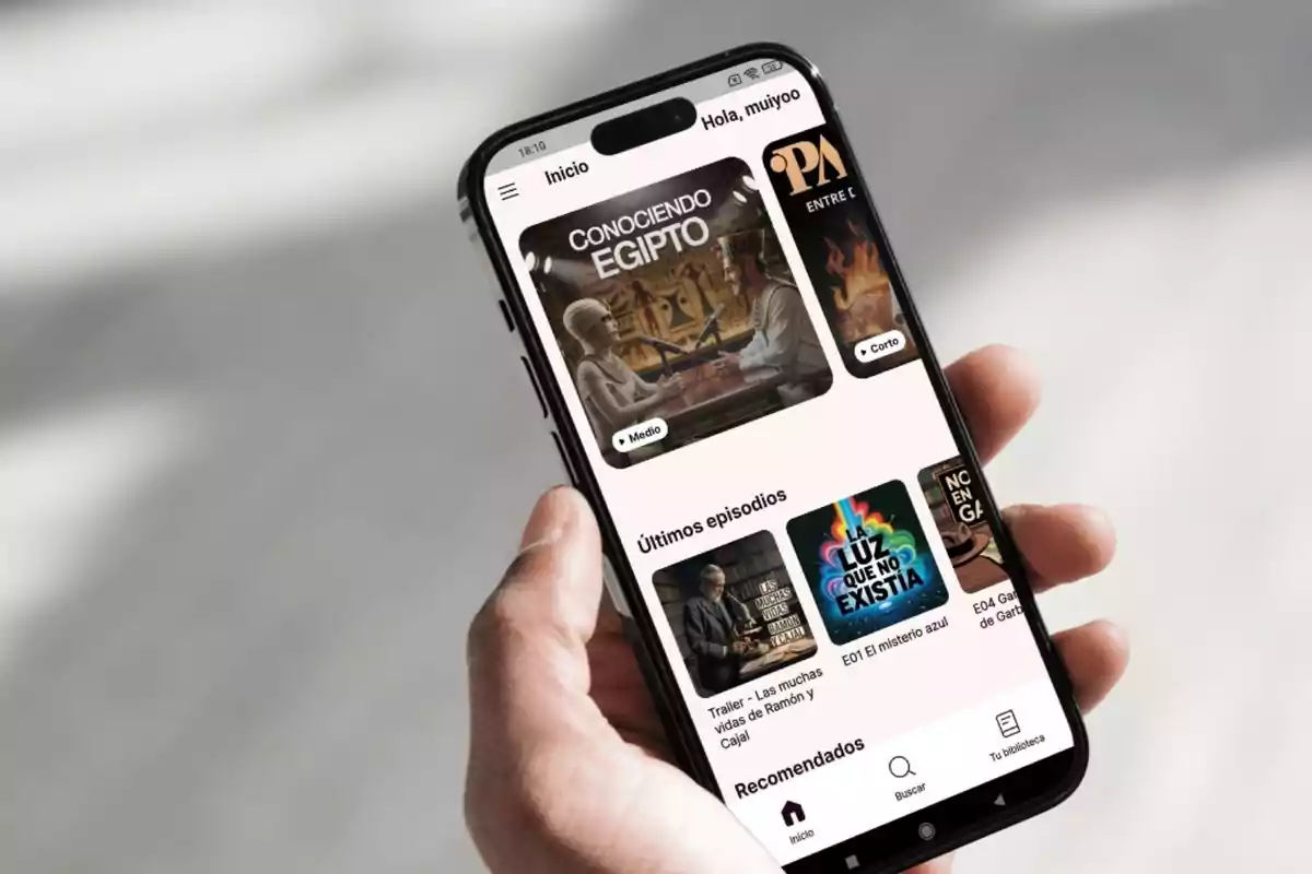Persona sosteniendo un teléfono móvil que muestra una aplicación de podcasts con diferentes episodios y recomendaciones en la pantalla