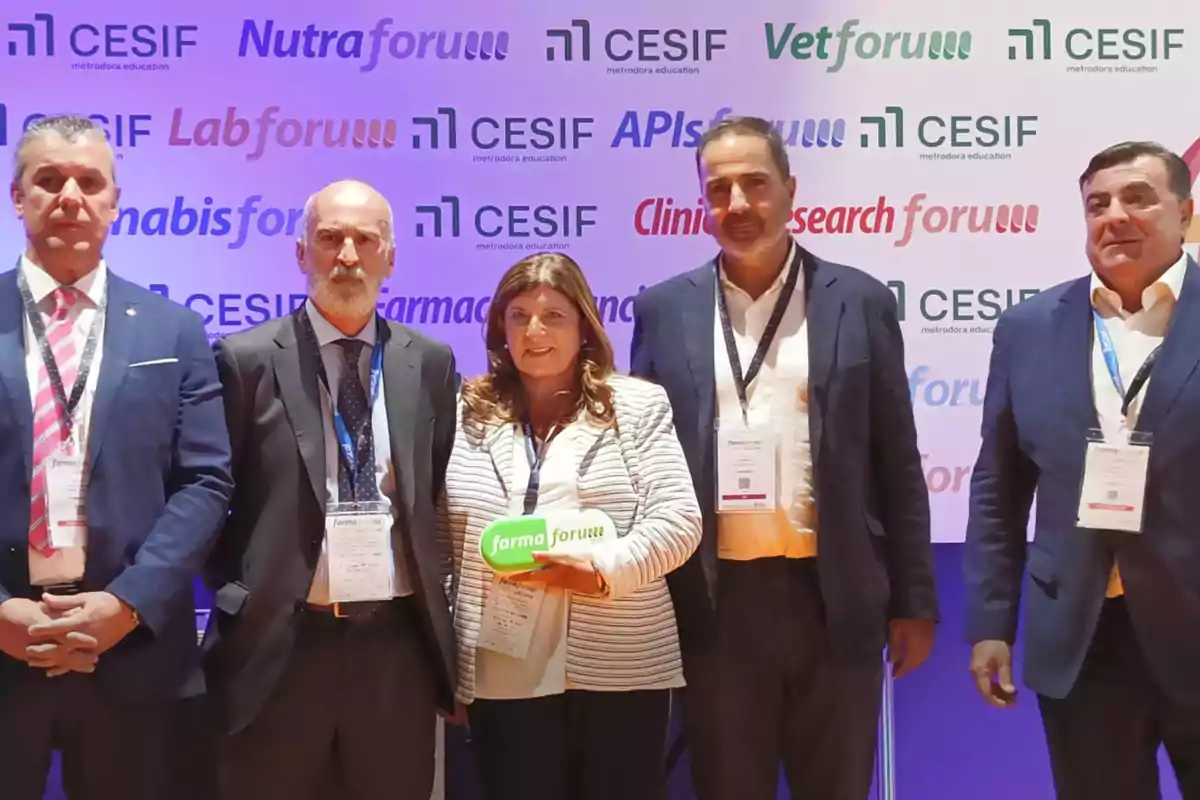 Cinco personas posan en un evento profesional con acreditaciones colgadas al cuello y un fondo con logotipos de Farmaforum y CESIF, una mujer en el centro sostiene un objeto verde con el nombre del evento.