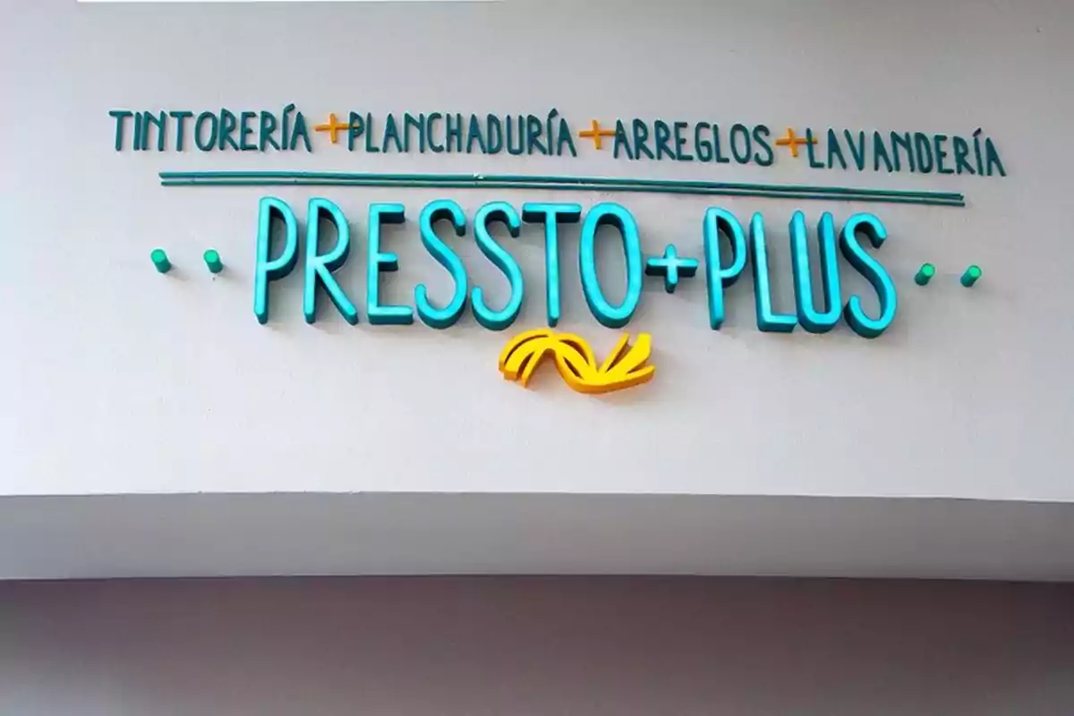 Fachada de una tienda con el letrero Pressto Plus en letras grandes y color turquesa, acompañado de servicios como tintorería, planchaduría, arreglos y lavandería en la parte superior