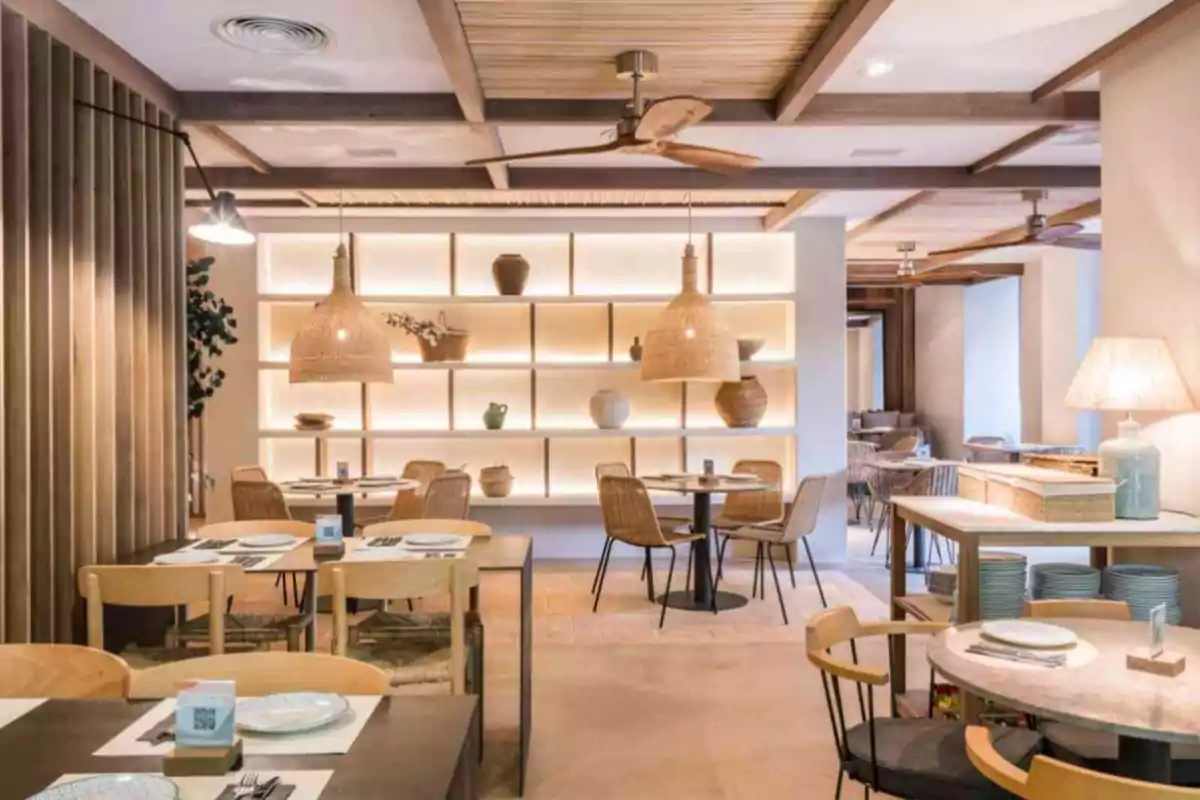 Restaurante moderno con decoración de madera, lámparas colgantes de mimbre, estantería iluminada con jarrones y mesas preparadas para recibir comensales