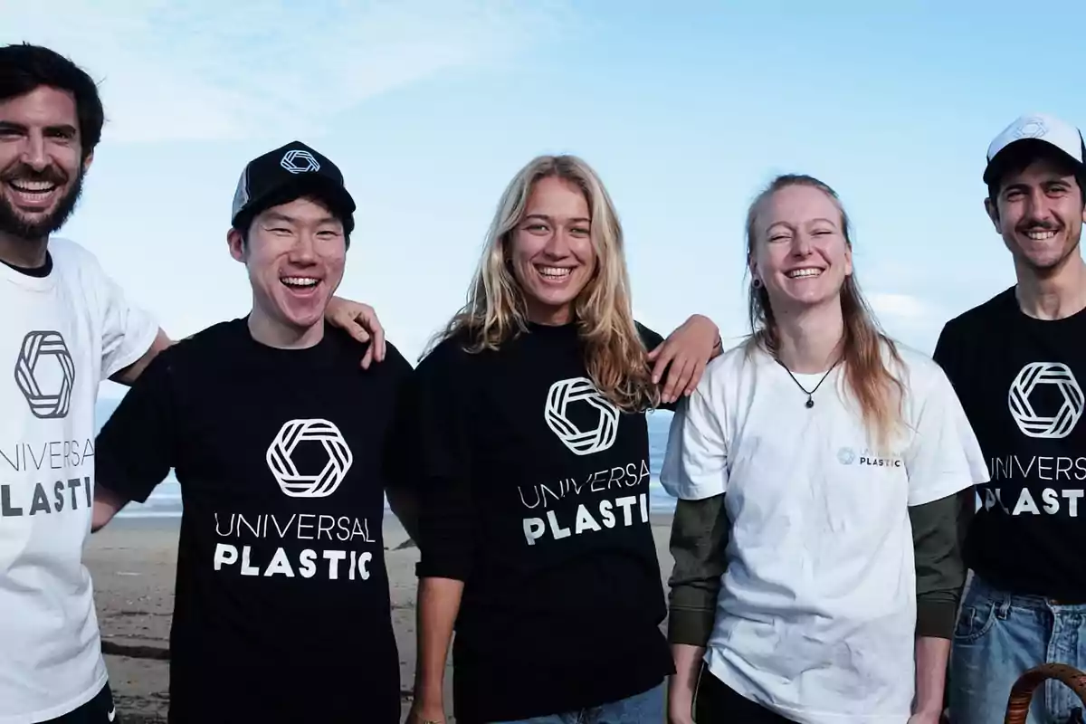 Cinco personas jóvenes sonríen mientras posan juntas en la playa usando camisetas de Universal Plastic