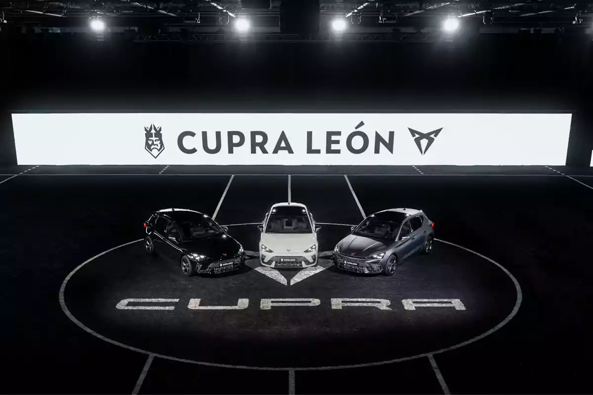 Tres autos Cupra León estacionados en un círculo iluminado con un letrero grande de fondo que dice Cupra León Tres autos Cupra León estacionados en un círculo iluminado con un letrero grande de fondo que dice Cupra León