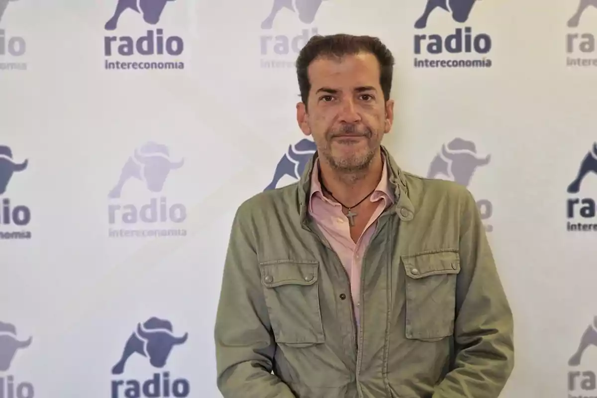 Hombre de cabello corto y barba recortada con chaqueta verde y camisa rosa posando frente a un fondo con el logo de Radio Intereconomía.