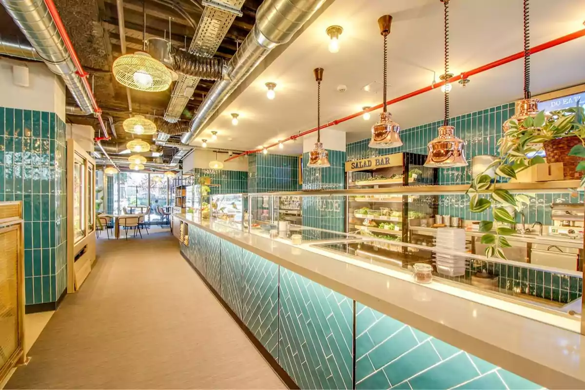 Restaurante moderno con barra de ensaladas, decoración en tonos turquesa, lámparas colgantes y ambiente luminoso