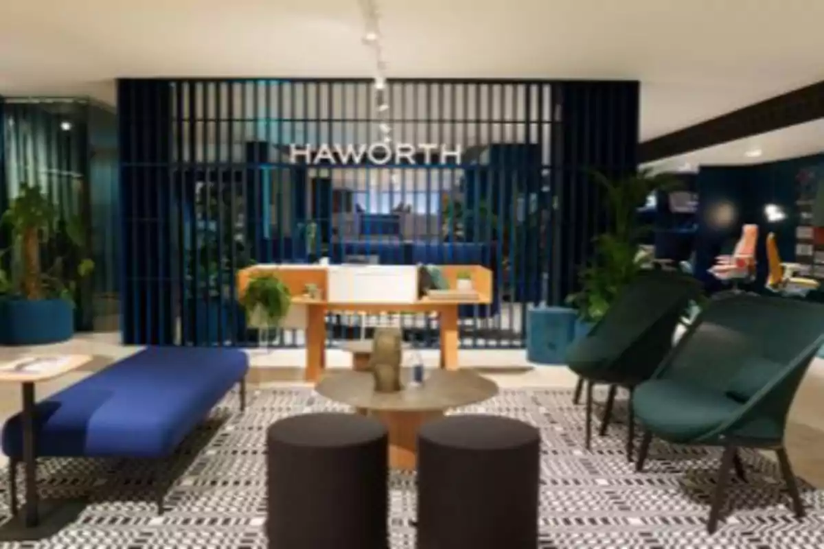 Sala de espera moderna con sillones verdes, banco azul, mesas bajas y plantas decorativas frente a un panel azul con el letrero Haworth