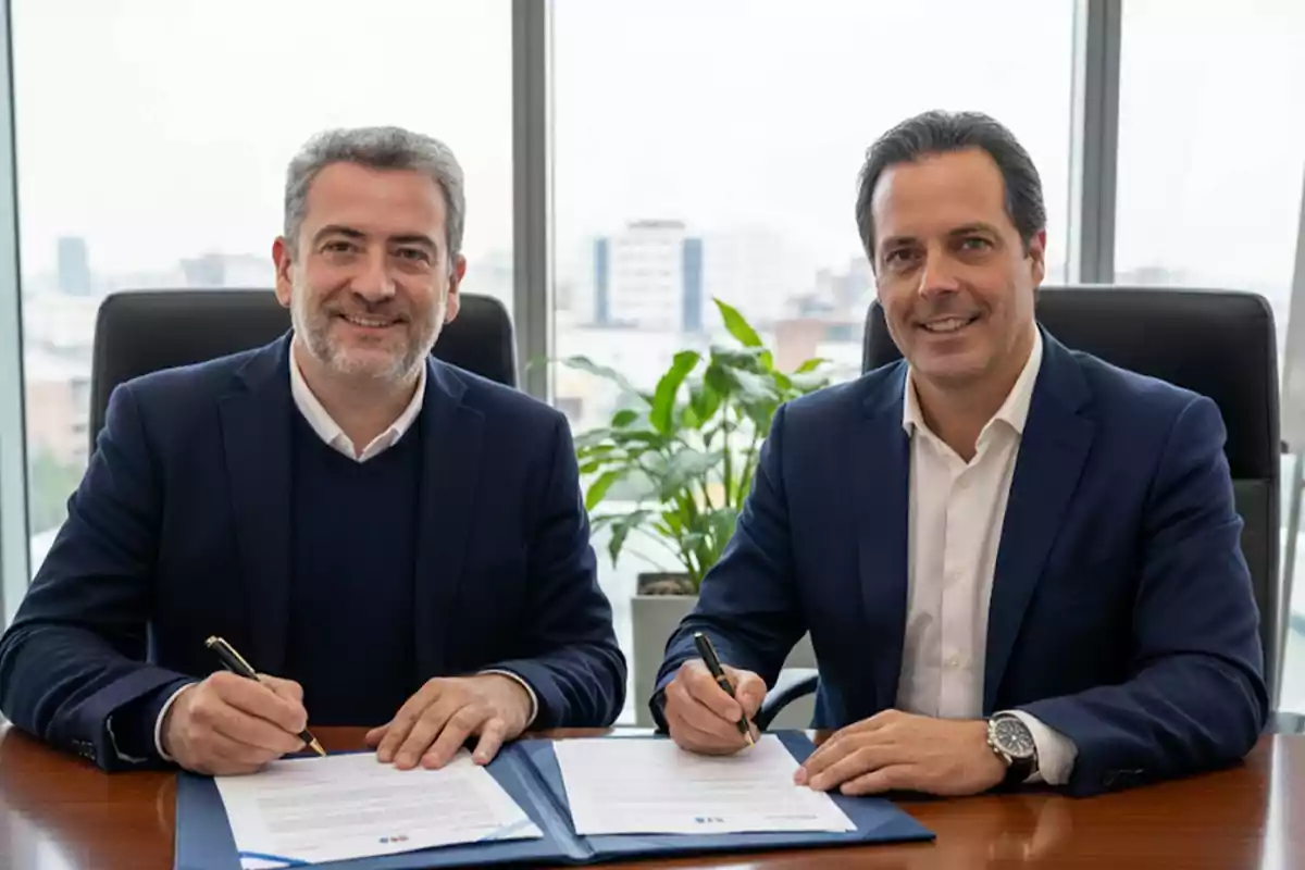 Dos hombres de negocios sonríen mientras firman documentos en una oficina moderna con una planta al fondo y una vista urbana a través de la ventana