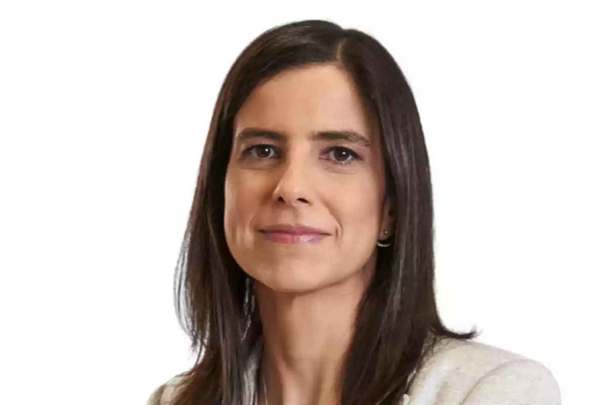 Mujer de cabello lacio y oscuro con expresión seria, vestida con saco claro y fondo blanco