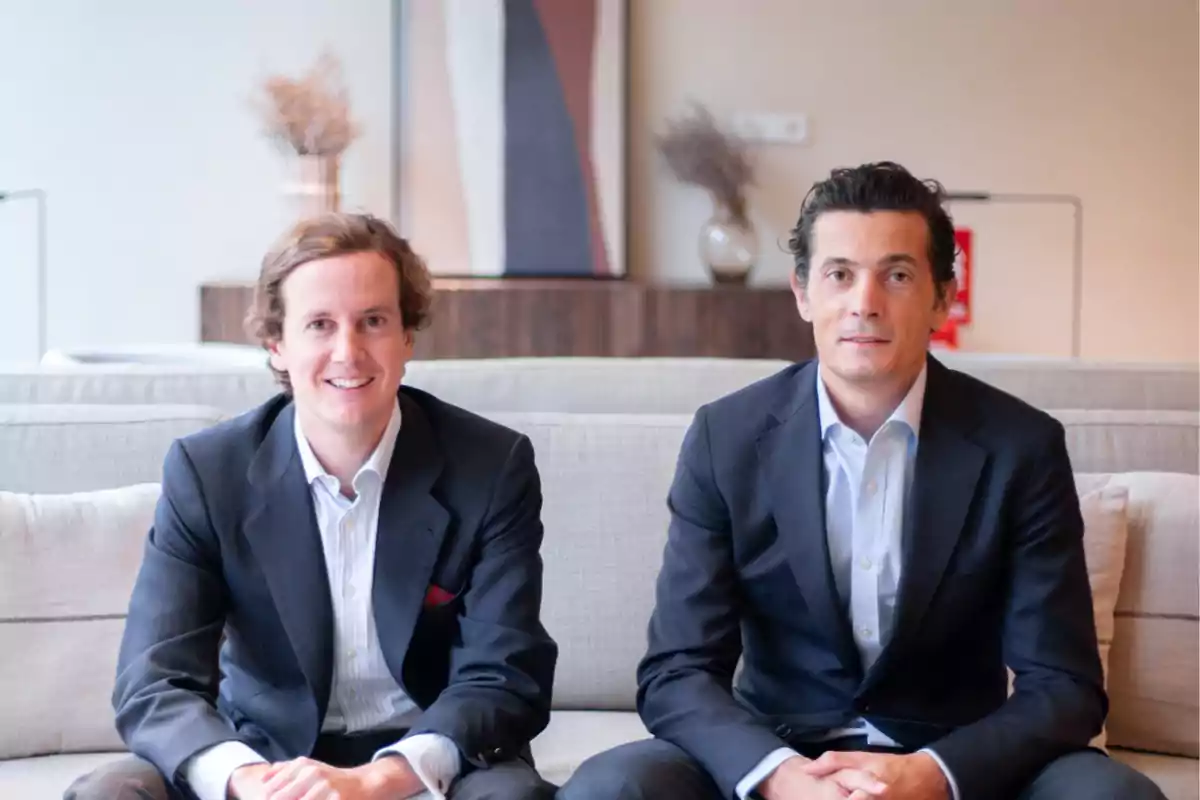 Dos hombres con traje sentados en un sofá en una sala moderna con decoración minimalista Dos hombres con traje sentados en un sofá en una sala moderna con decoración minimalista