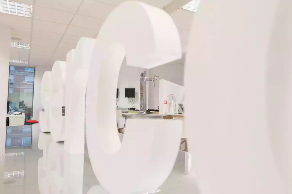 Letras blancas gigantes dentro de una oficina moderna con escritorios y monitores al fondo Letras blancas gigantes dentro de una oficina moderna con escritorios y monitores al fondo