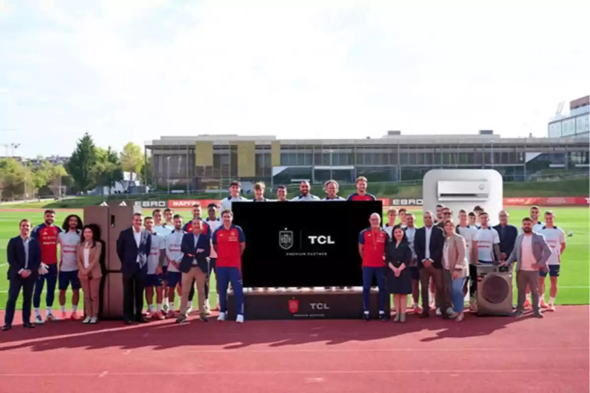 Grupo de personas posando en una cancha de fútbol junto a electrodomésticos y una pantalla con el logo de TCL