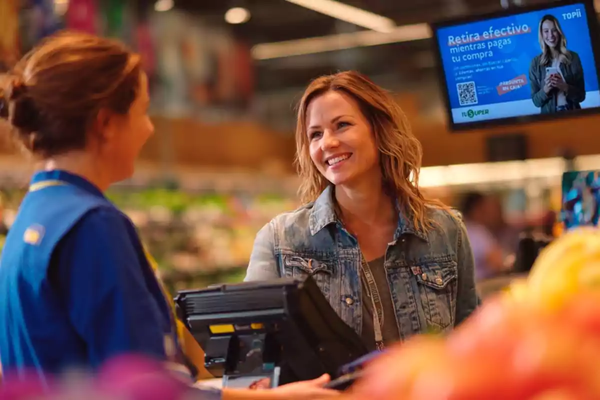 Mujer sonriendo mientras paga en la caja de un supermercado y conversa con la cajera