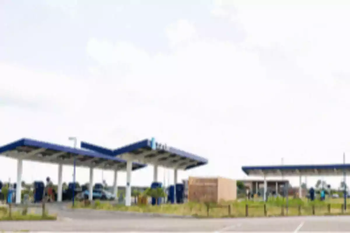 Estación de servicio con techo azul y varios autos estacionados en un día soleado