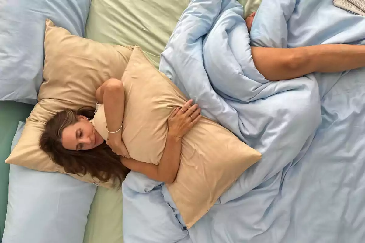 Mujer acostada en una cama con sábanas azules abrazando una almohada beige