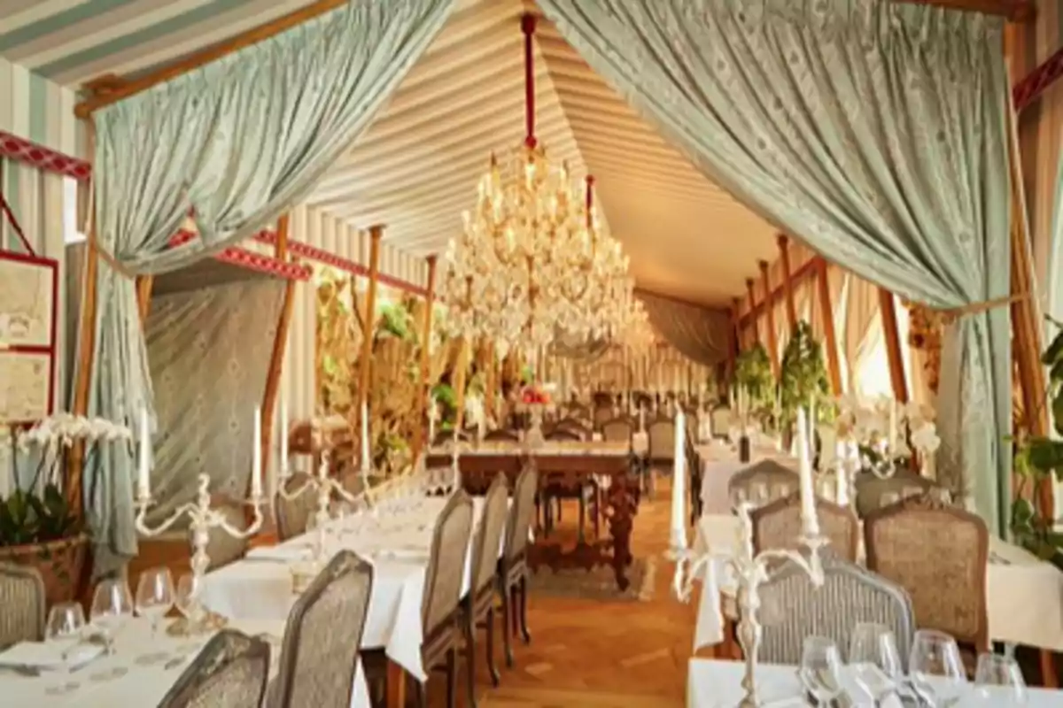 Restaurante elegante con mesas vestidas de manteles blancos, candelabros, cortinas de tela y grandes lámparas de araña en el techo