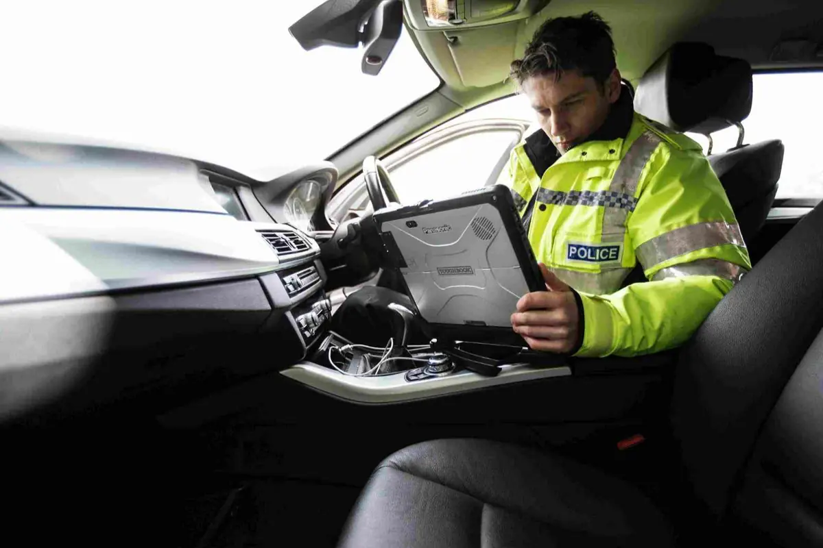 Policía con chaqueta reflectante usando una computadora portátil dentro de un coche patrulla