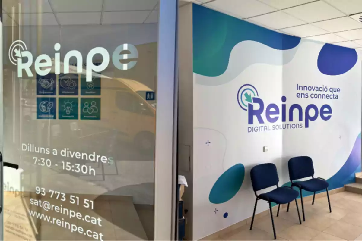 Entrada de una oficina de Reinpe Digital Solutions con información de contacto y horario en la puerta de cristal y un mural interior con el logo de la empresa, dos sillas azules y el lema Innovació que ens connecta