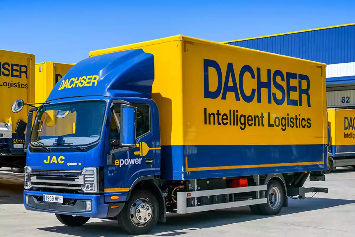 Camión de reparto eléctrico de la empresa Dachser estacionado en un centro logístico con otros vehículos similares al fondo Camión de reparto eléctrico de la empresa Dachser estacionado en un centro logístico con otros vehículos similares al fondo