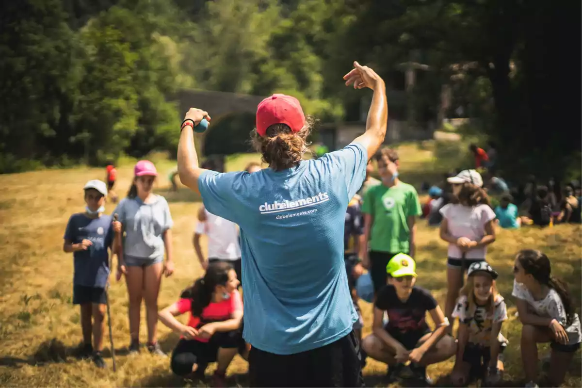 Persona con camiseta azul y gorra roja dirige a un grupo de niños al aire libre en un día soleado Persona con camiseta azul y gorra roja dirige a un grupo de niños al aire libre en un día soleado