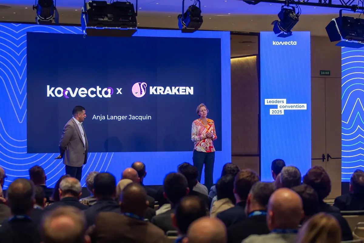Dos personas presentan en un escenario frente a una audiencia en una convención empresarial con pantallas azules que muestran los logotipos de Kovecta y Kraken y el nombre Anja Langer Jacquin